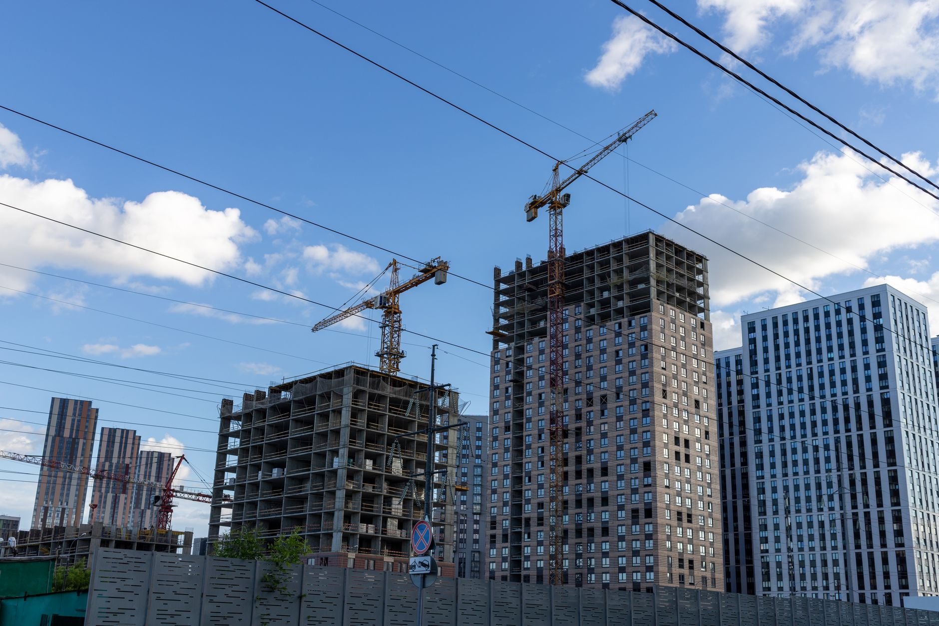 City skyline with modern buildings and construction cranes under a blue sky.